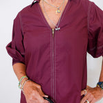 Person wearing a burgundy zip-up shirt holding a black handbag against a white background