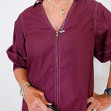 Person wearing a burgundy zip-up shirt holding a black handbag against a white background