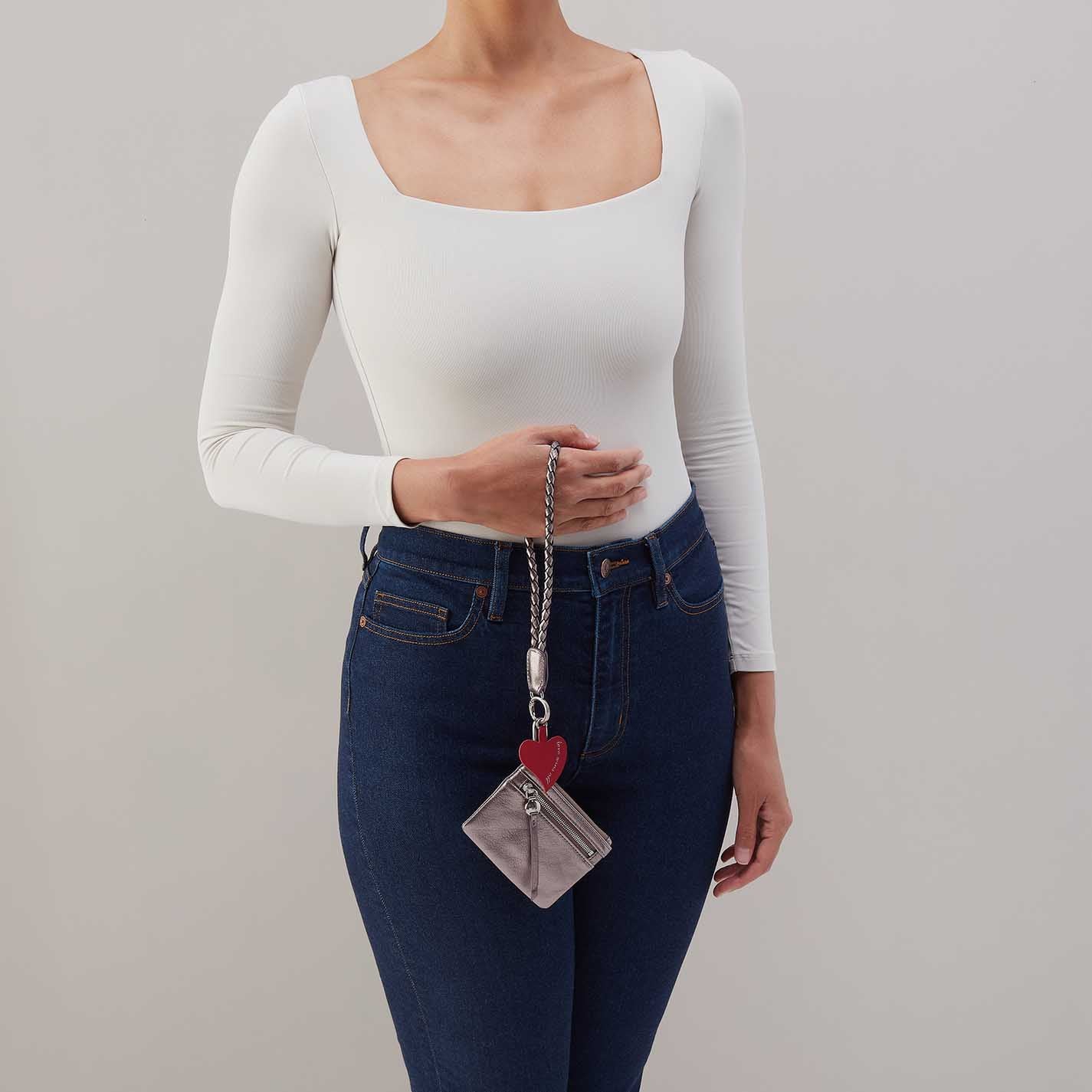 woman holding the Hobo lasso phone wristlet in metallic leather, color pewter spur against a white background. 