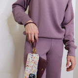 woman modeling the lasso phone wristlet in pebbled leather mulberry glaze color against a white background. 