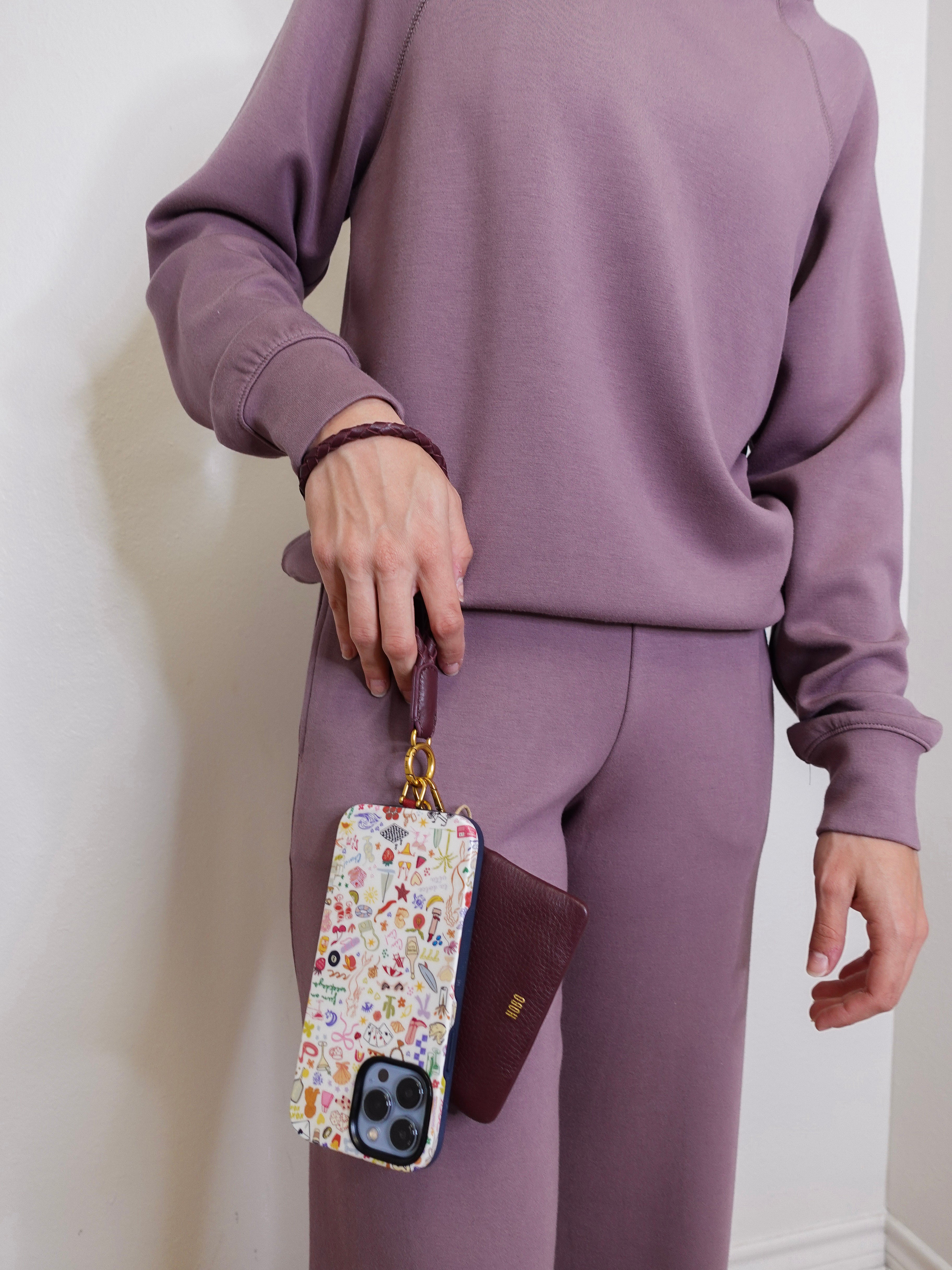 woman modeling the lasso phone wristlet in pebbled leather mulberry glaze color against a white background. 