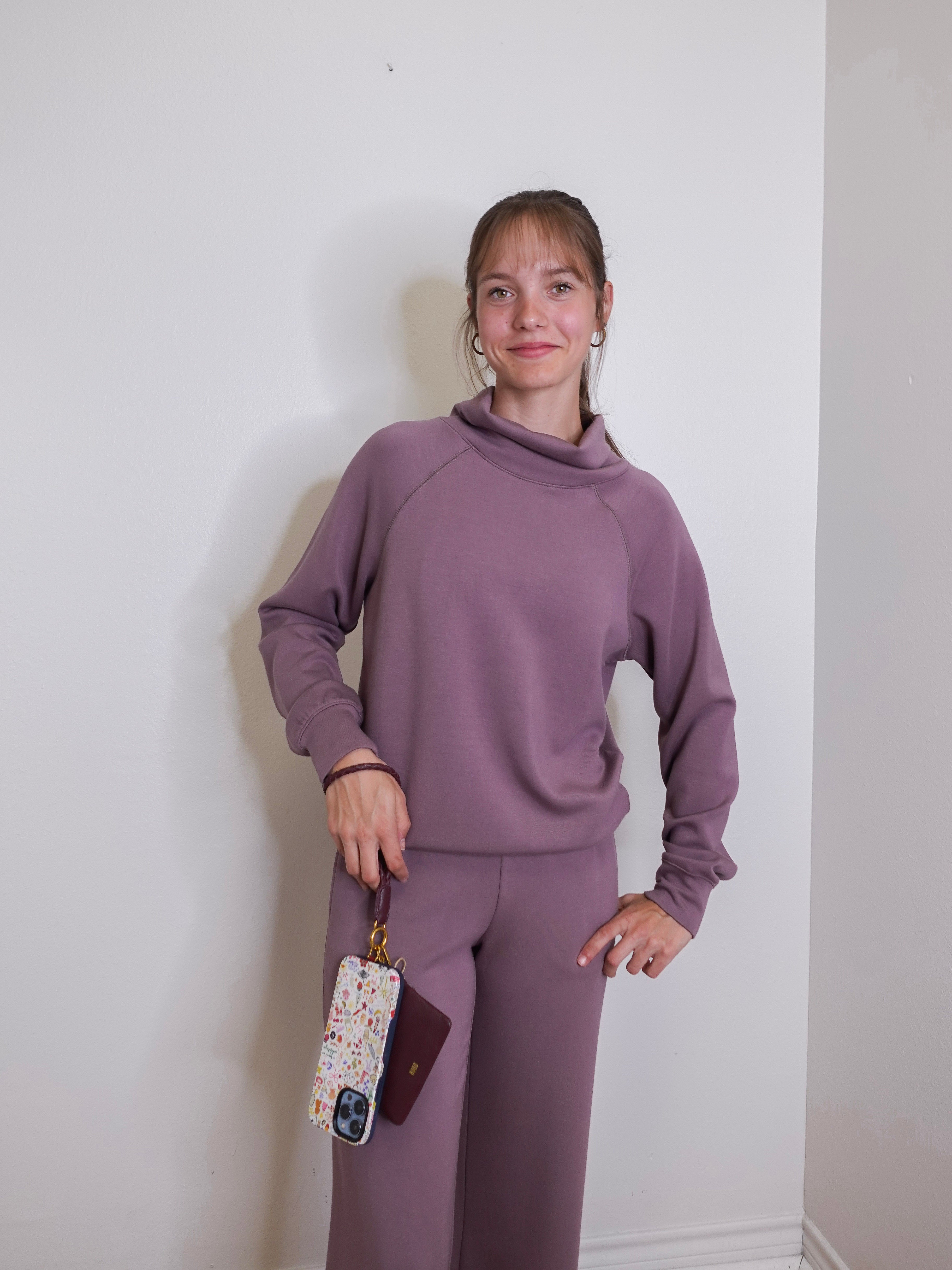 woman modeling the lasso phone wristlet in pebbled leather mulberry glaze color against a white background. 