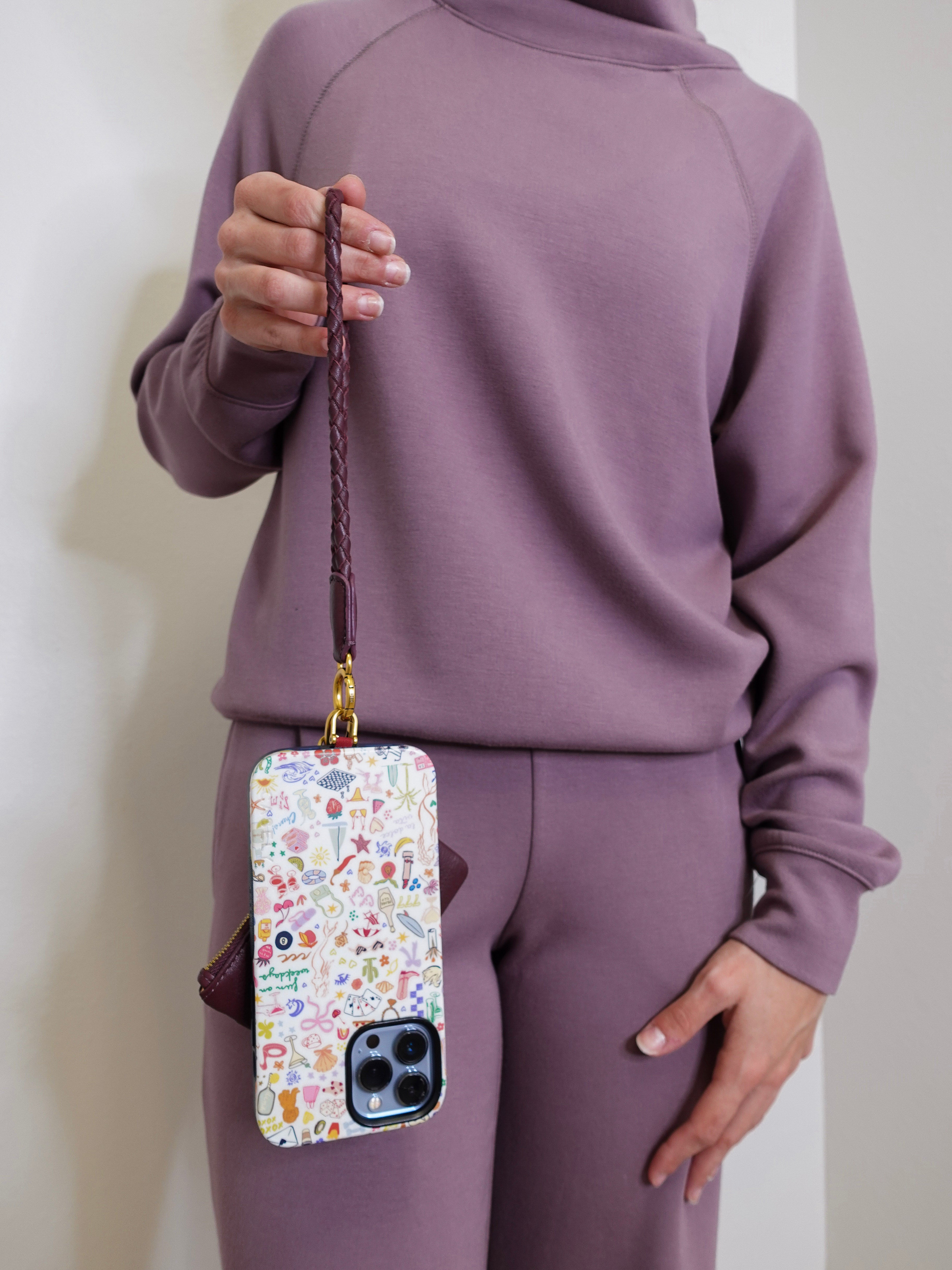 woman modeling the lasso phone wristlet in pebbled leather mulberry glaze color against a white background. 