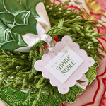 Decorative green wreath with a 'Sophie Noble' tag on a patterned surface.
