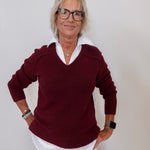 Woman wearing a burgundy sweater with a white collar against a plain background