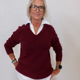 Woman wearing a burgundy sweater with a white collar against a plain background
