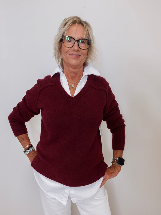 Woman wearing a burgundy sweater with a white collar against a plain background