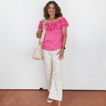 Woman wearing a pink top and white polka dot pants against a white wall.