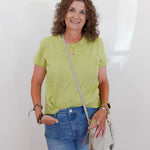 Woman wearing a green shirt and blue jeans, holding a beige handbag against a white background