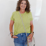Woman wearing a green shirt and blue jeans, holding a beige handbag against a white background