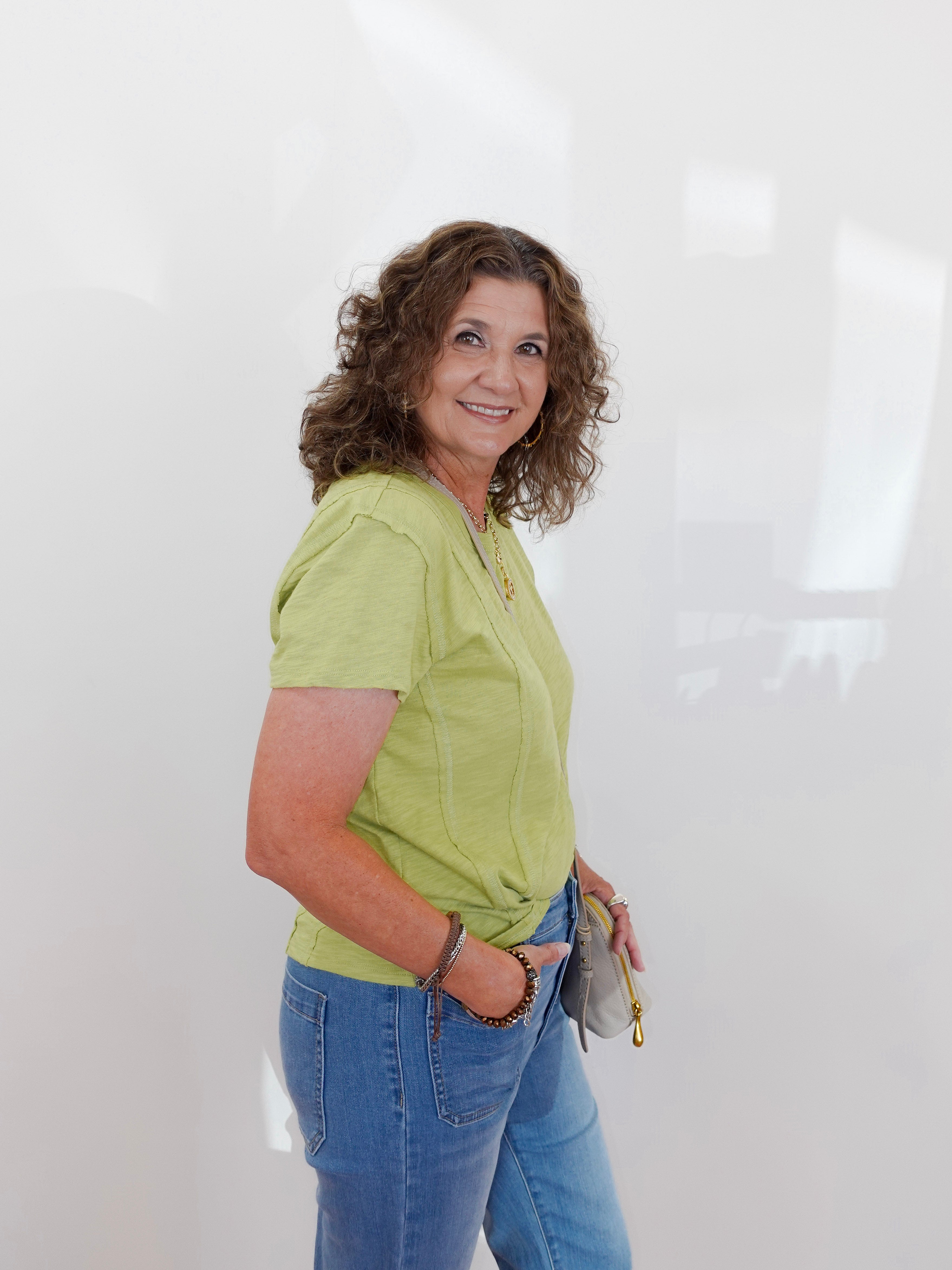 Woman wearing a green shirt and blue jeans against a white background