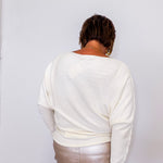 Person wearing a white sweater and light-colored pants against a plain background