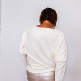 Person wearing a white sweater and light-colored pants against a plain background