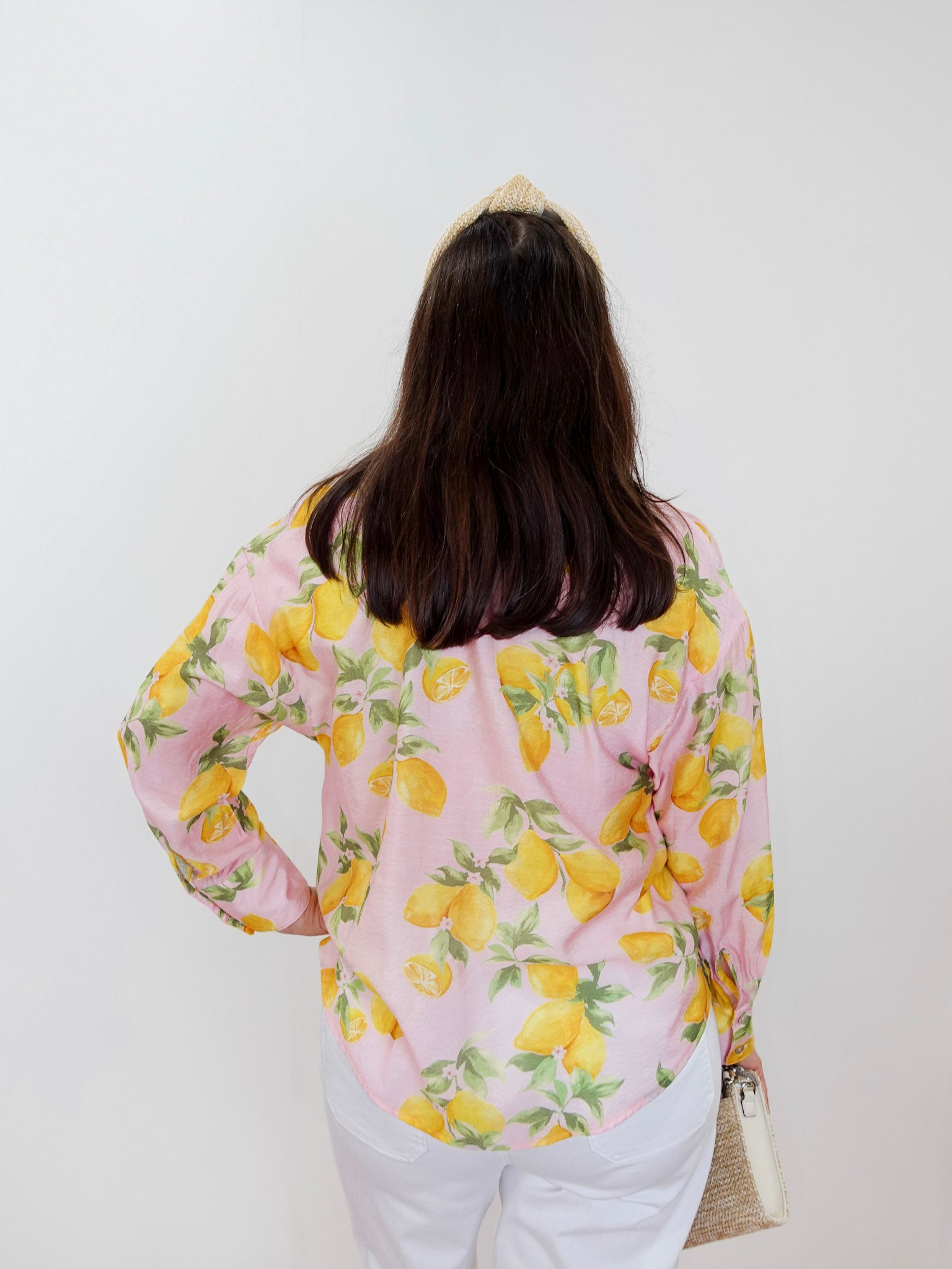 Person wearing a pink blouse with lemon print against a white background