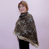 Person wearing a leopard print poncho with fur trim against a plain background
