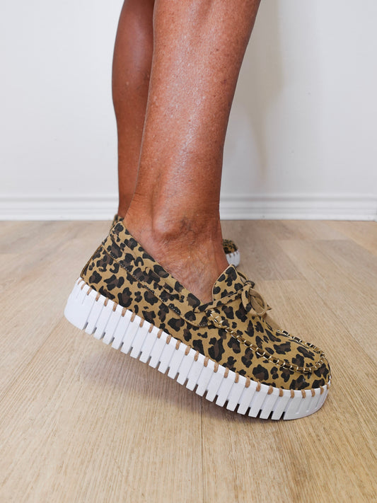 Leopard print sneakers with white soles worn indoors on a wooden floor.