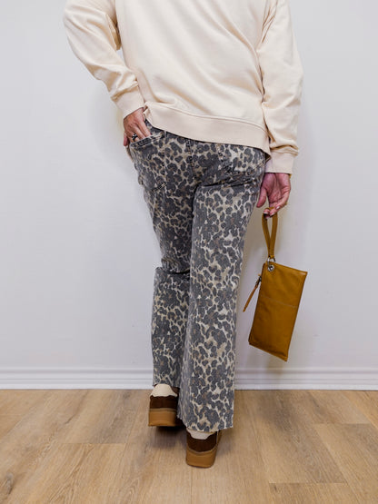 Person wearing a beige sweater and patterned pants holding a brown bag against a white wall.