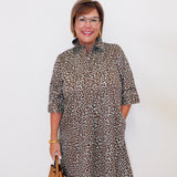 Woman wearing a leopard print dress holding a brown handbag against a white background