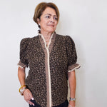 Woman wearing a leopard print blouse with a white wall background