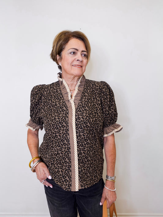 Woman wearing a leopard print blouse with a white wall background
