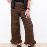 Person wearing leopard print pants and black loafers against a white wall.
