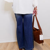 Person wearing blue jeans and a white top, holding a brown handbag with a tag.