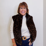 Woman wearing a leopard print vest over a white shirt with blue jeans against a plain background