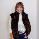 Woman wearing a leopard print vest over a white shirt with blue jeans against a plain background