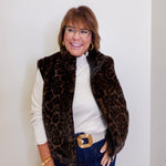 Woman wearing a leopard print vest over a white shirt with blue jeans against a plain background