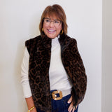 Woman wearing a leopard print vest over a white shirt with blue jeans against a plain background
