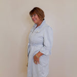 Woman wearing a light blue trench coat against a plain wall.