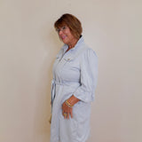 Woman wearing a light blue trench coat against a plain wall.
