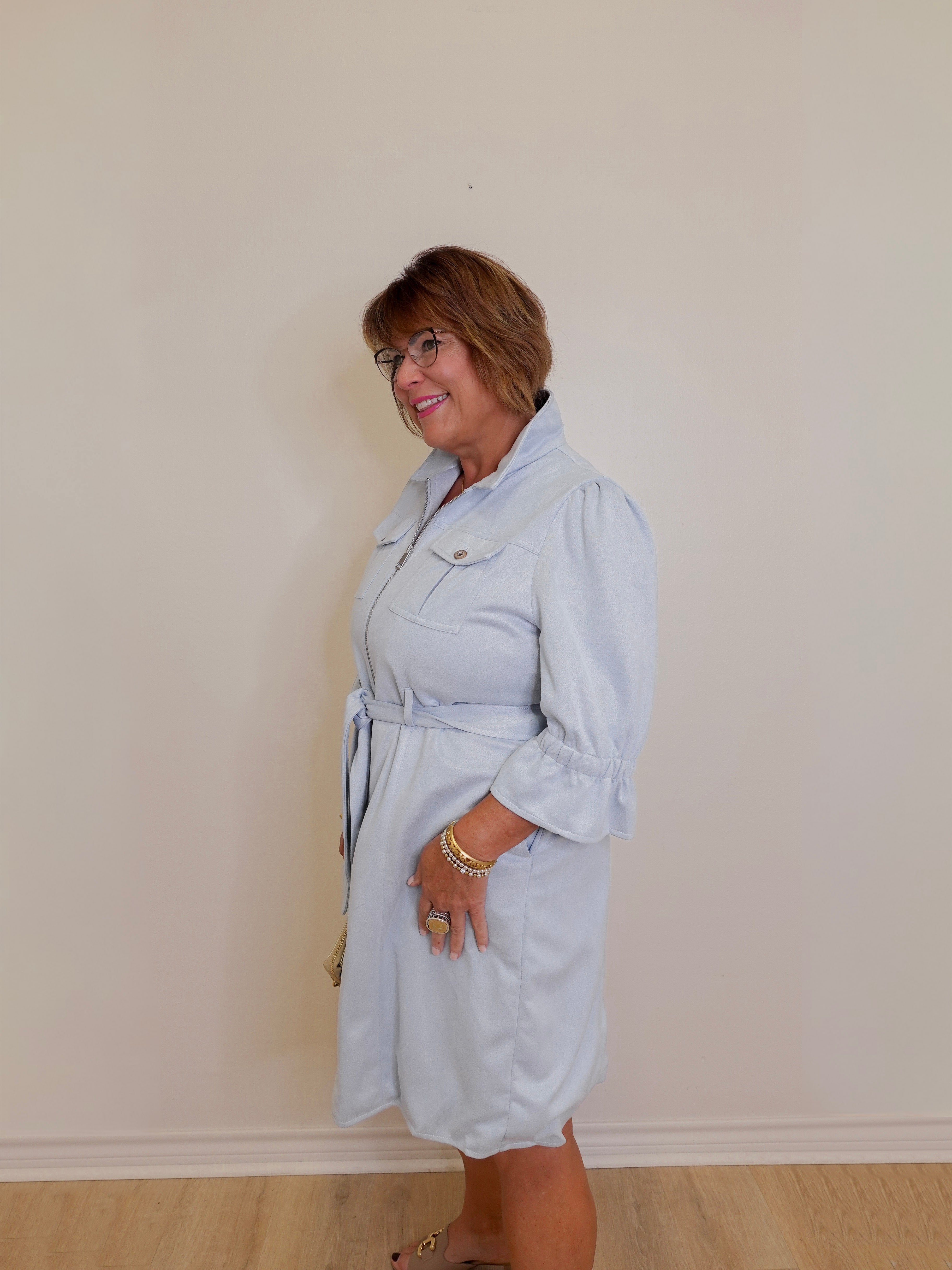 Woman wearing a light blue trench coat against a plain wall.