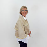 Person wearing a beige jacket with white trim on a plain background