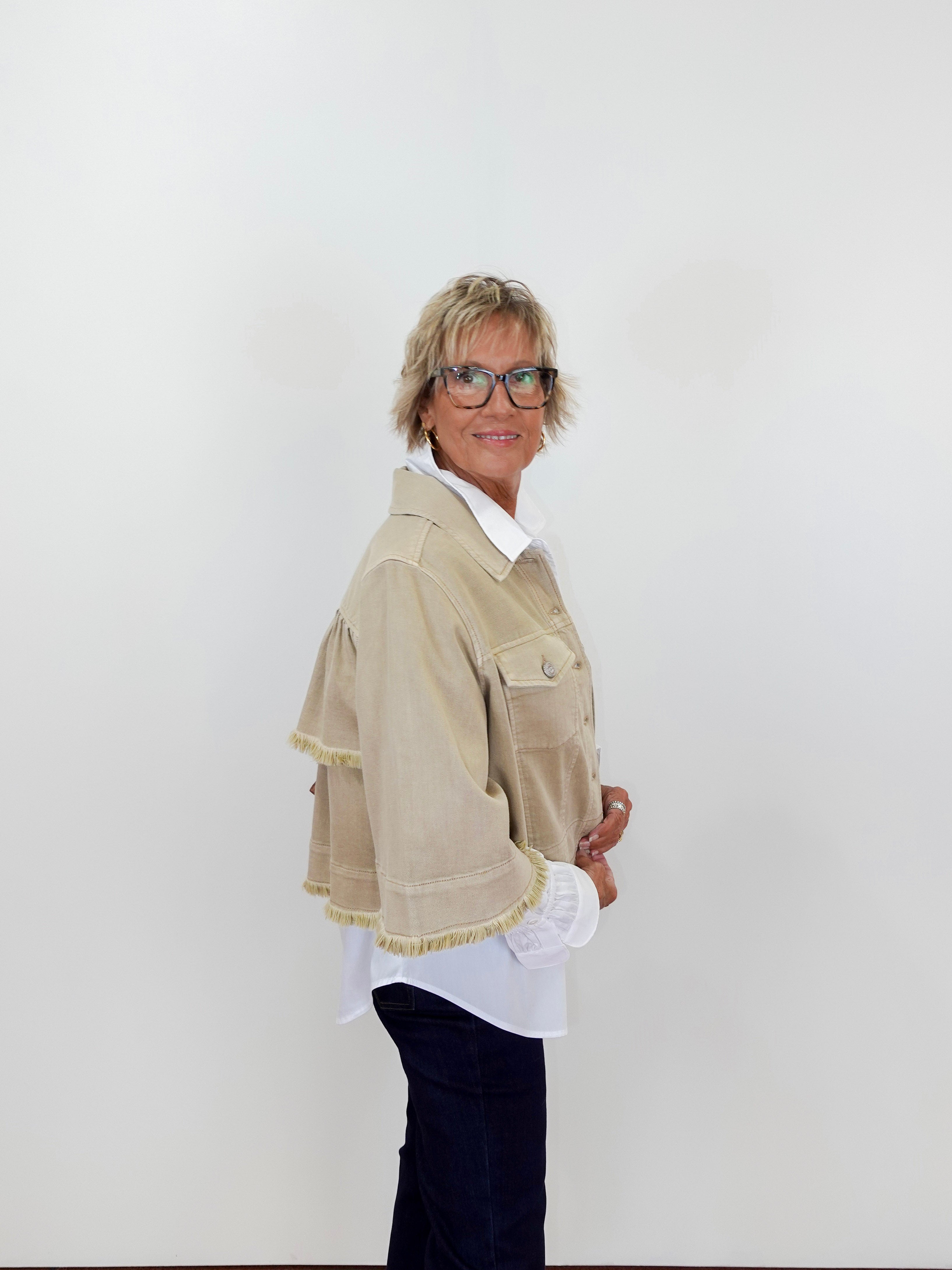 Person wearing a beige jacket with white trim on a plain background