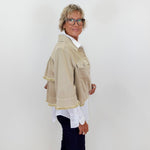 Person wearing a beige jacket with white trim against a plain background