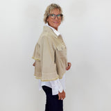 Person wearing a beige jacket with white trim against a plain background