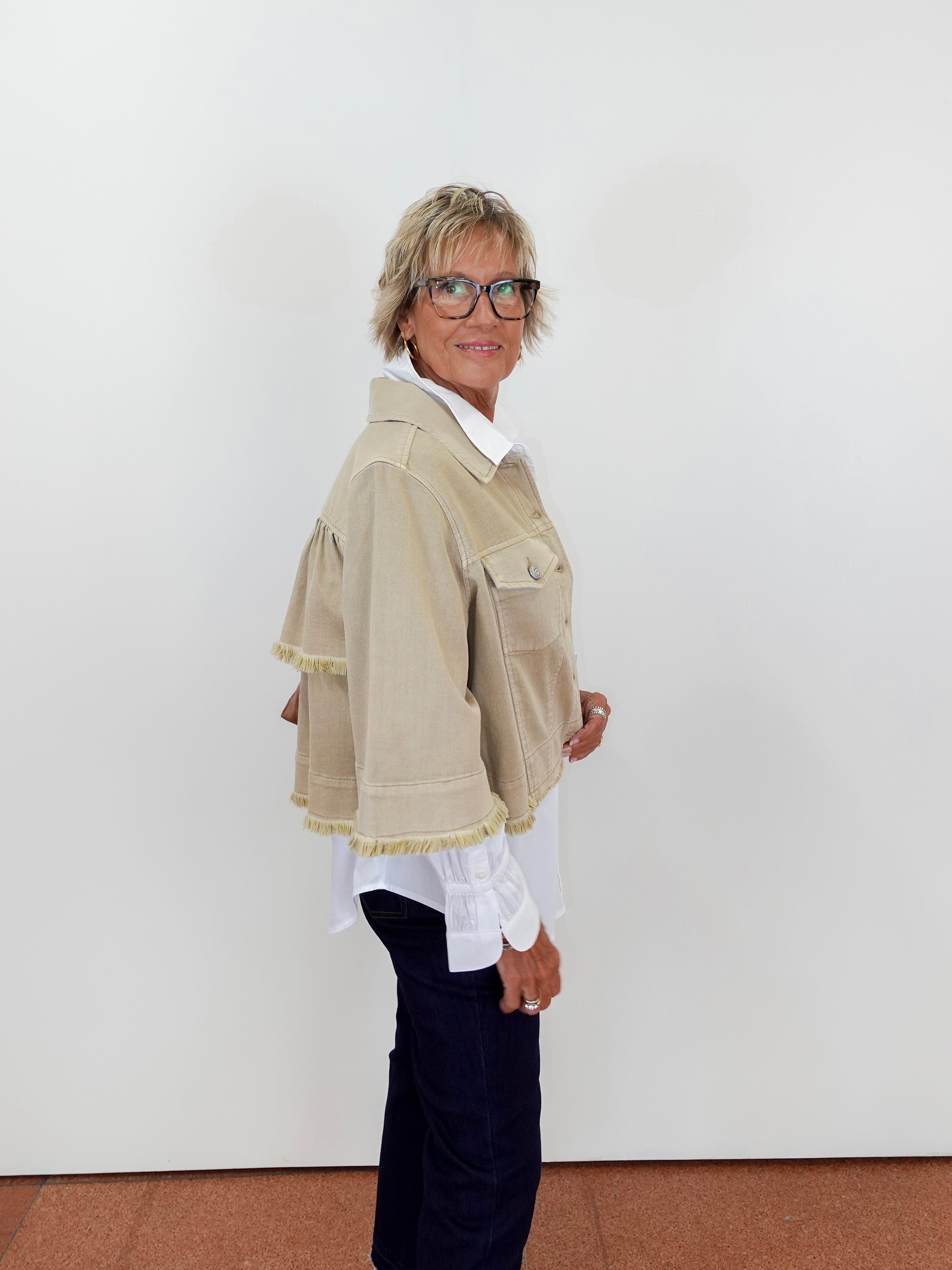 Person wearing a beige jacket with white trim against a plain background