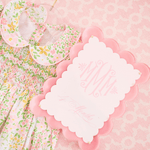 Floral baby bib and blanket with a pink scalloped edge card on a pink patterned background