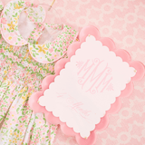 Floral baby bib and blanket with a pink scalloped edge card on a pink patterned background