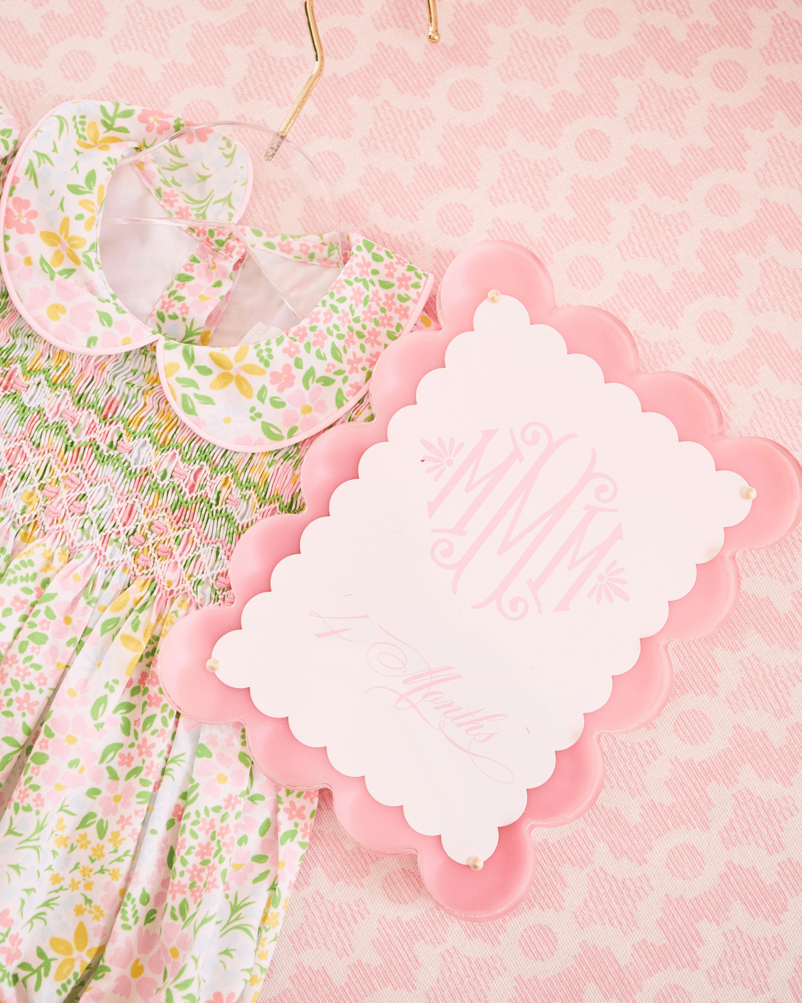 Floral baby bib and blanket with a pink scalloped edge card on a pink patterned background