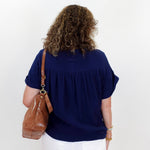 Person wearing a navy blue top and white pants with a brown bag on a white background