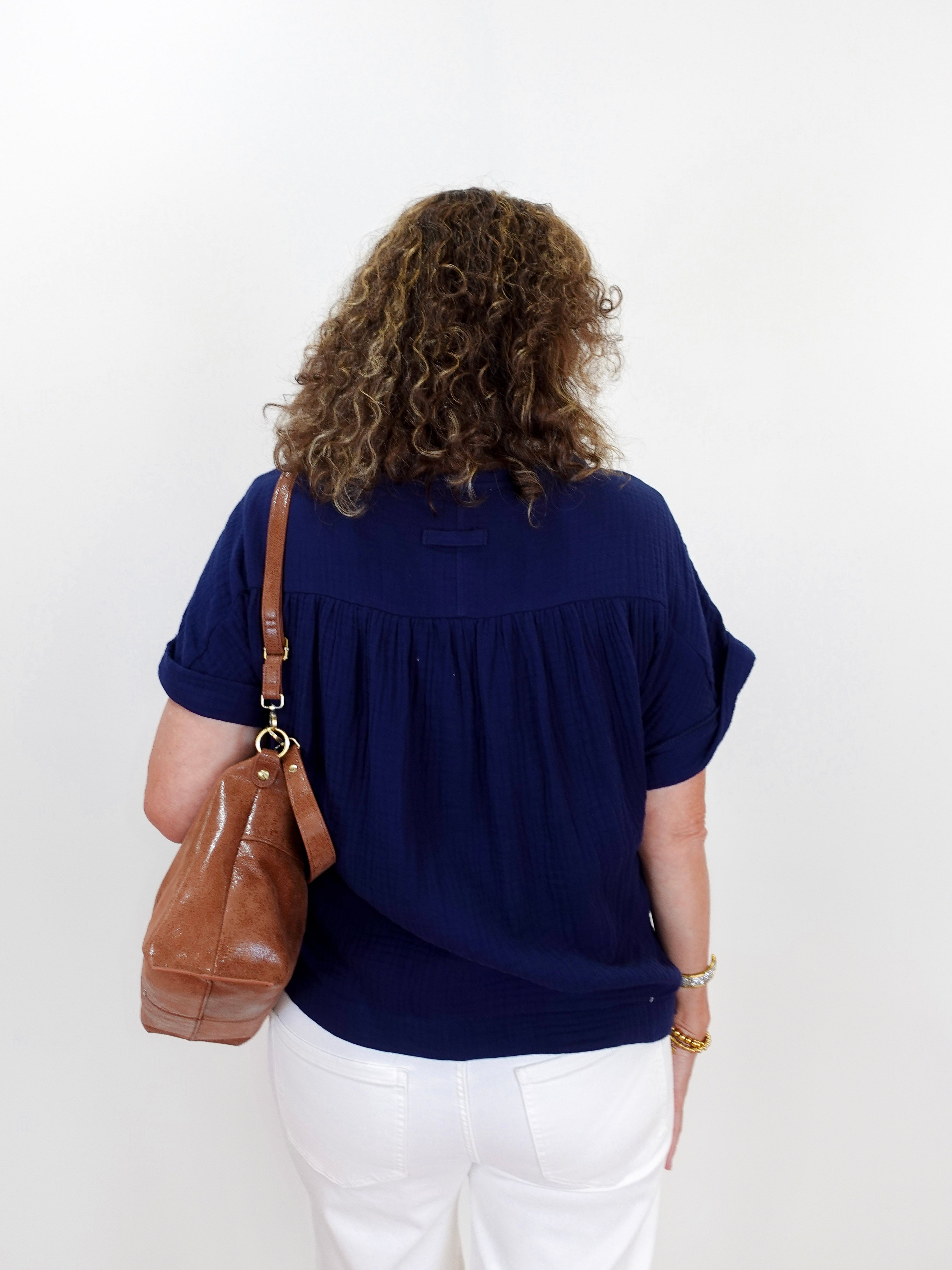 Person wearing a navy blue top and white pants with a brown bag on a white background