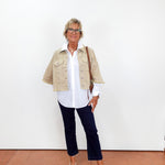 Person wearing a beige jacket, white shirt, navy pants, and white shoes on a plain background