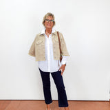 Person wearing a beige jacket, white shirt, navy pants, and white shoes on a plain background