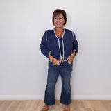 Woman wearing a blue patterned jacket and jeans standing against a white wall.
