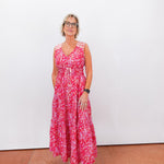 Woman wearing a red floral dress standing against a white wall.