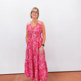 Woman wearing a red floral dress standing against a white wall.