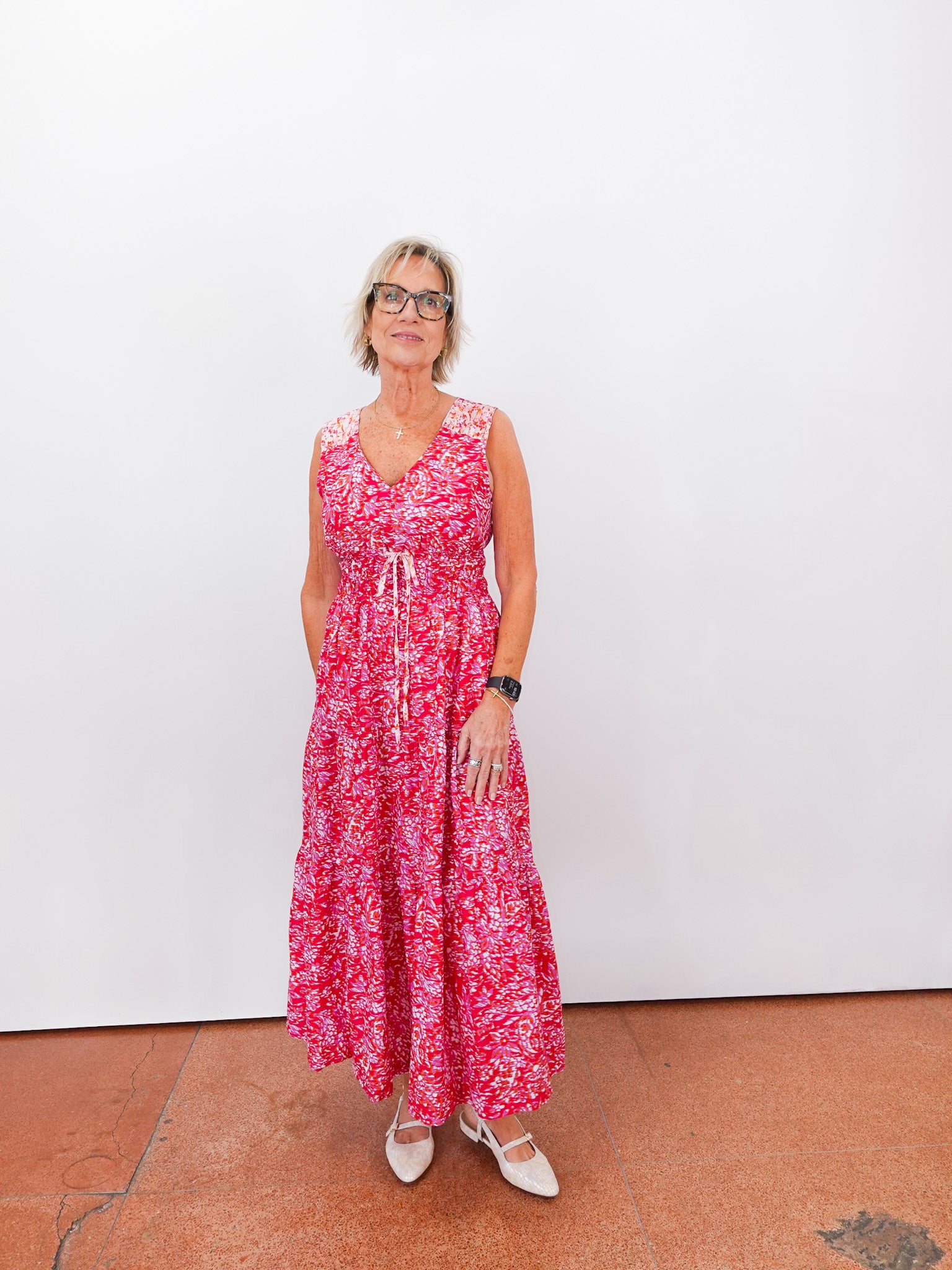 Woman wearing a red floral dress standing against a white wall.
