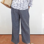 Person wearing a white shirt with black geometric pattern and gray wide-leg pants, standing on a brown floor.